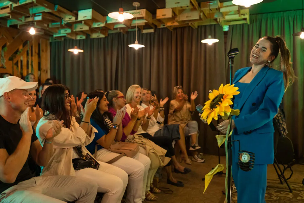 Artista sonriendo feliz mientras el público del Secret Concert aplaude con ganas en una sala bonita y cálida